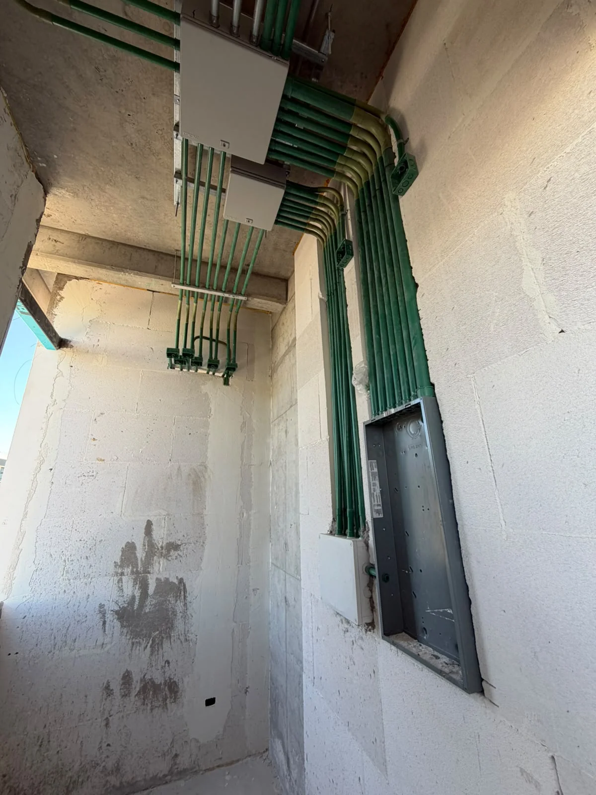 Canalizaciones eléctricas verdes que llegan a un tablero en un muro en obra.