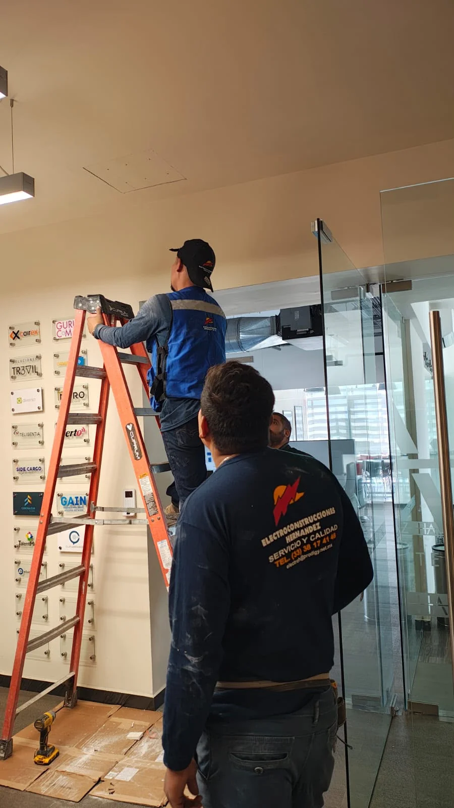 Dos personas con uniforme de Electroconstrucciones Hernández trabajando en una instalación interior.