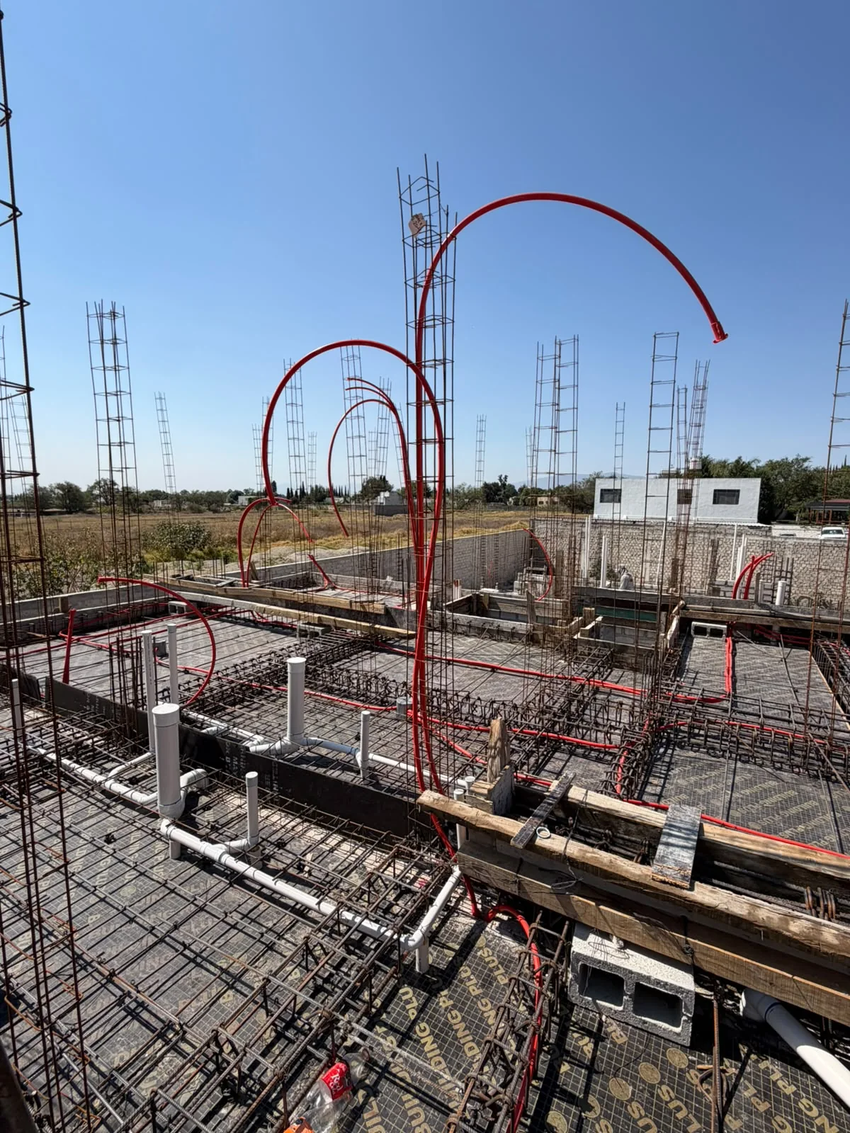 Tuberías rojas y armados de acero sobre la cimbra de una losa en construcción.