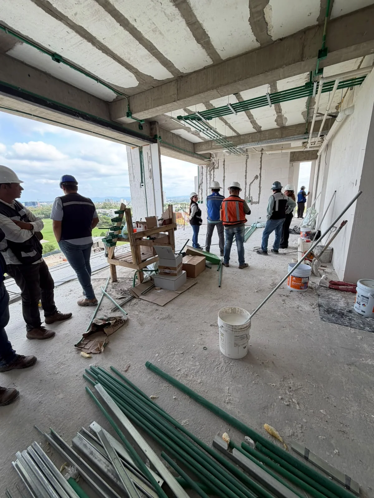 Grupo de personas con cascos y chalecos en un inmueble en construcción, bajo canalizaciones eléctricas.
