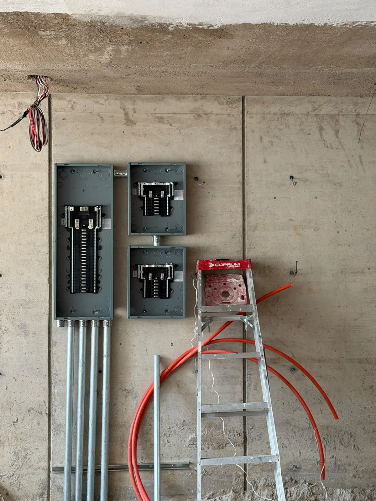 Tres tableros eléctricos sin tapa durante el montaje, con canalizaciones metálicas inferiores.